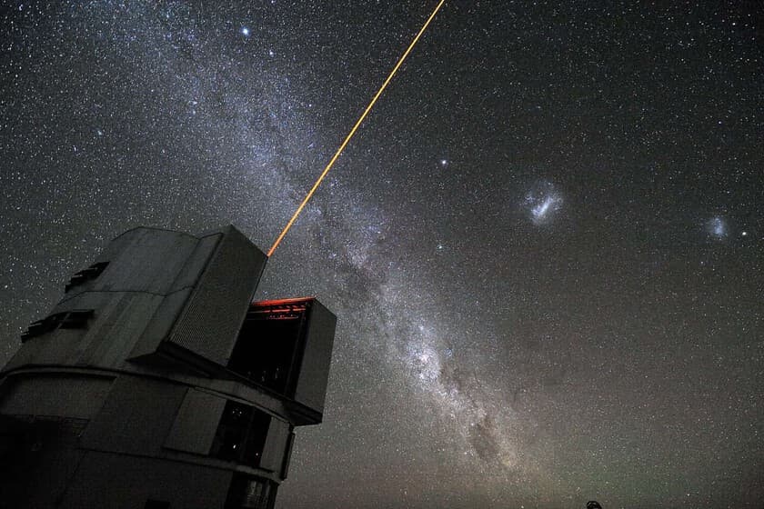 Vista nocturna del desierto de Atacama con el Observatorio Paranal iluminado y aerogeneradores al fondo