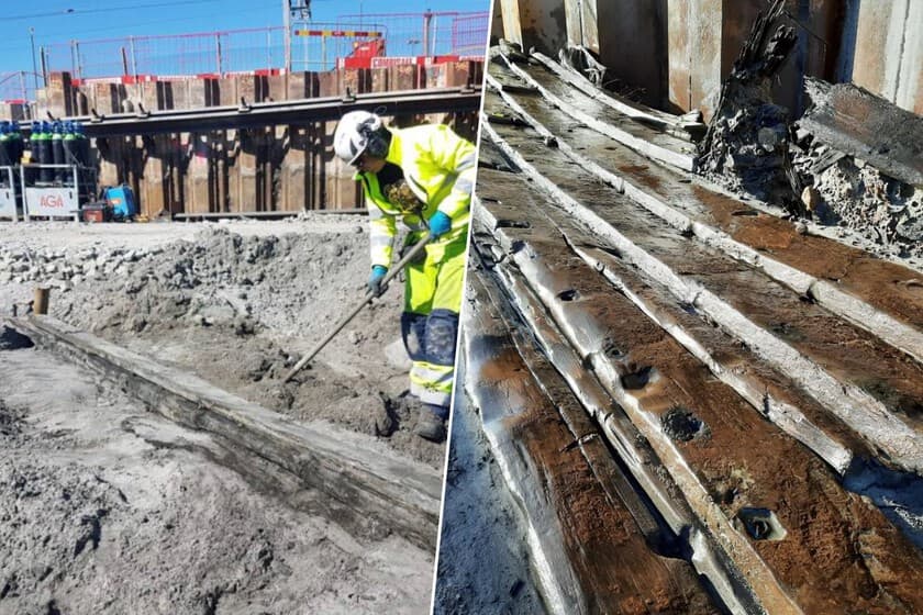 Obreros junto a restos de un barco de madera parcialmente enterrado en una excavación.