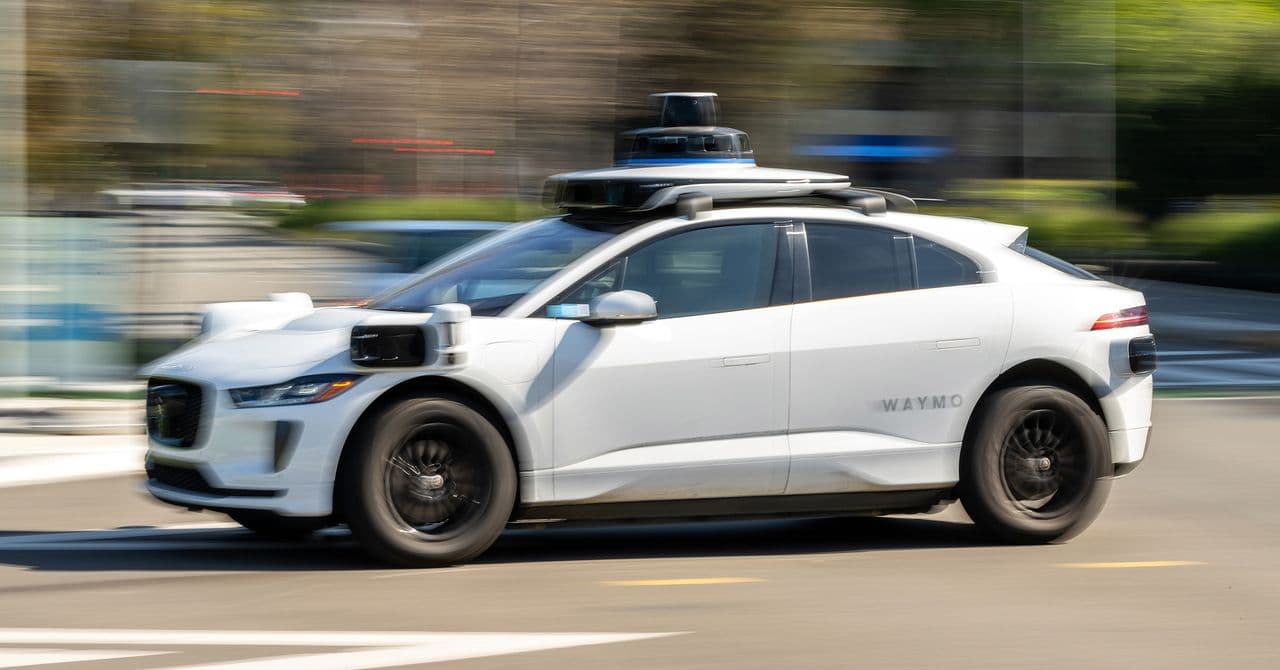 Un niño sentado solo en el asiento trasero de un Waymo, mirando por la ventana mientras el vehículo circula por una call