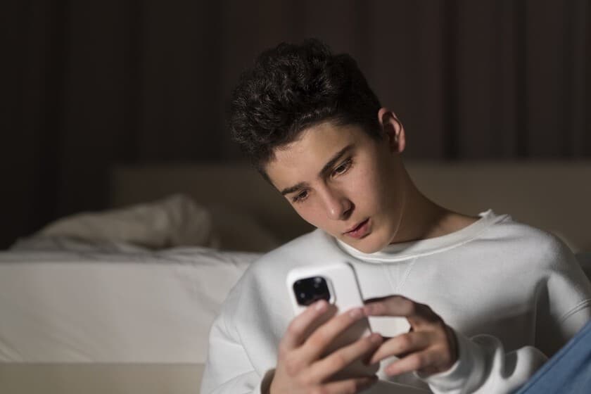 Joven mirando fijamente la pantalla de un smartphone en un entorno oscuro, con luz azul reflejada en su rostro