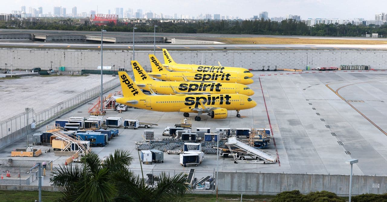 Un avión de Spirit Airlines en la pista de un aeropuerto al atardecer, con pasajeros mirando desde la terminal.