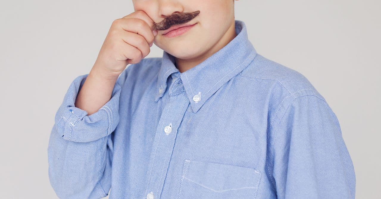Un niño sonriente con un bigote dibujado con lápiz de cejas frente a una pantalla de computadora