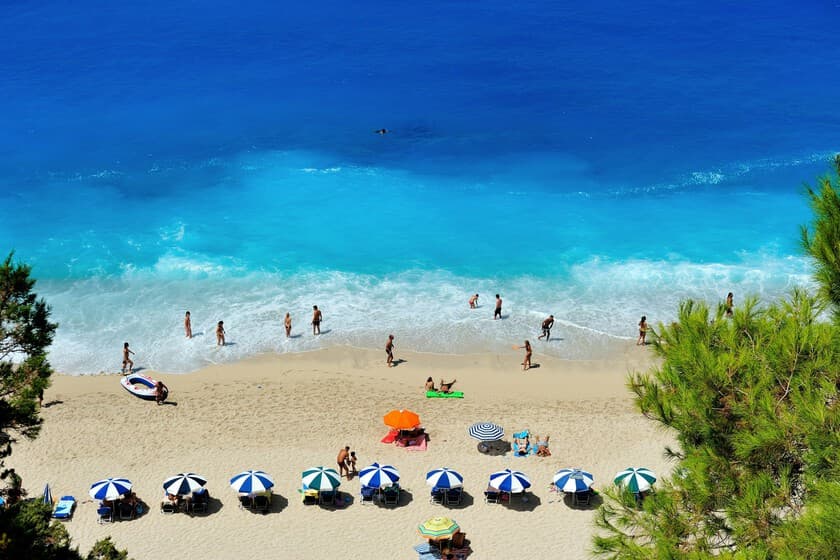 Playa griega vacía con mar turquesa y sin tumbonas, al atardecer
