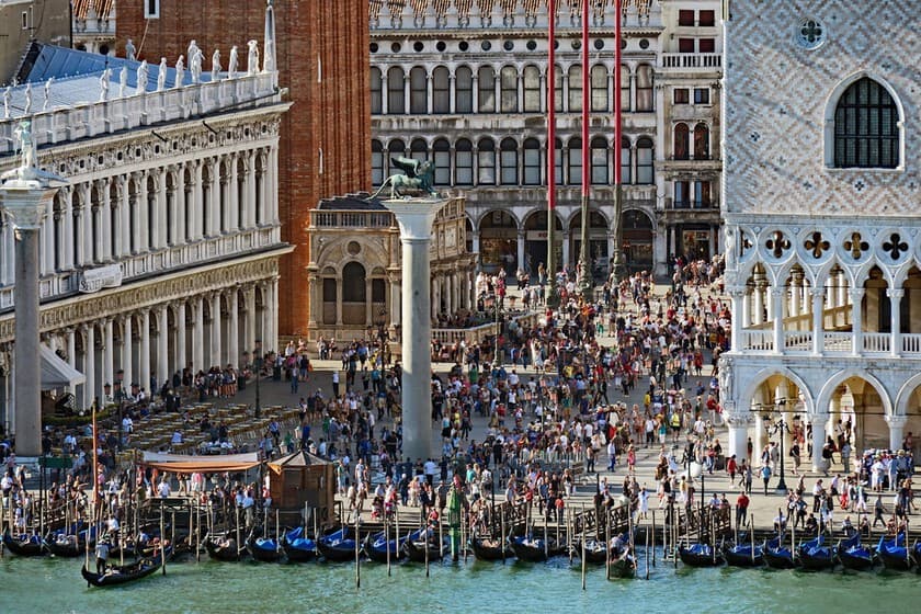 Turistas caminando por un puente veneciano con cartel de 'Entrada 10€' al fondo