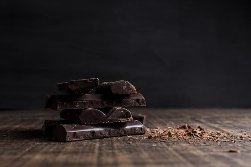Tableta de chocolate oscuro partida sobre una mesa de noche, junto a un reloj despertador marcando las 11 p.m.