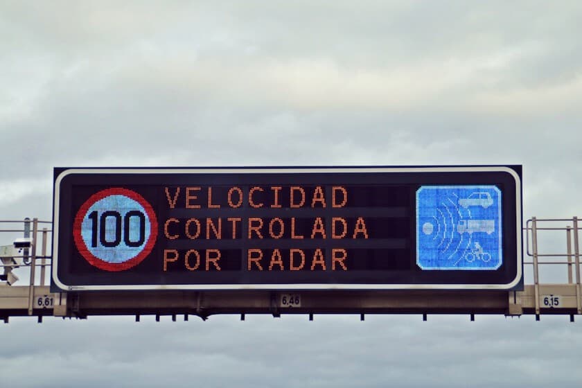 Carretera recta con señales de radar de tramo y un coche circulando, paisaje de Navarra al fondo