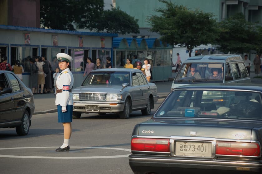 Calle abarrotada de coches en Pyongyang con edificios grises al fondo