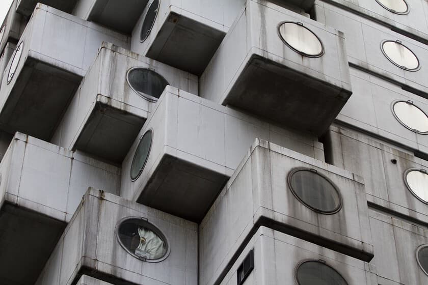 Fotografía de la Torre Nakagin en Tokio, con sus cápsulas de hormigón apiladas, algunas en estado de deterioro.