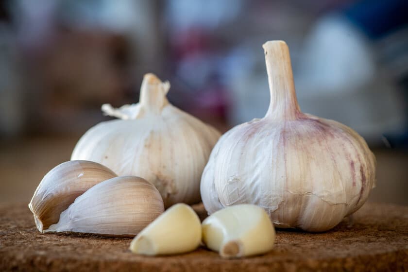 Ajo entero y dientes sobre tabla de madera, con fondo de cocina