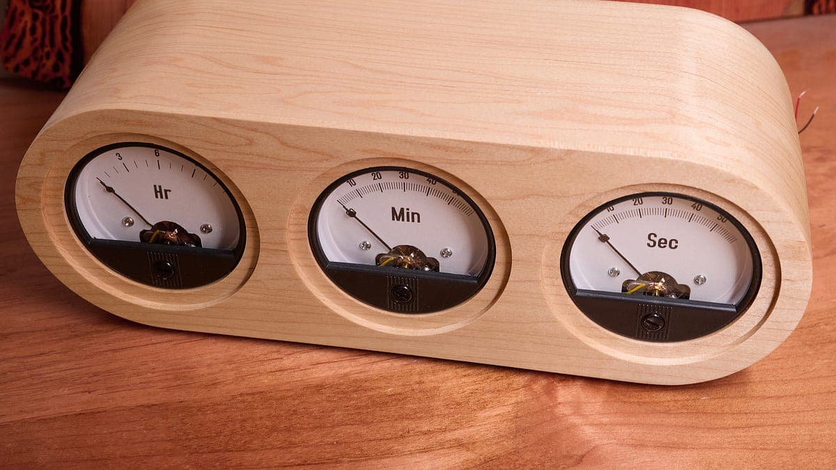 Voltímetro de aguja modificado funcionando como reloj, sobre una mesa de madera