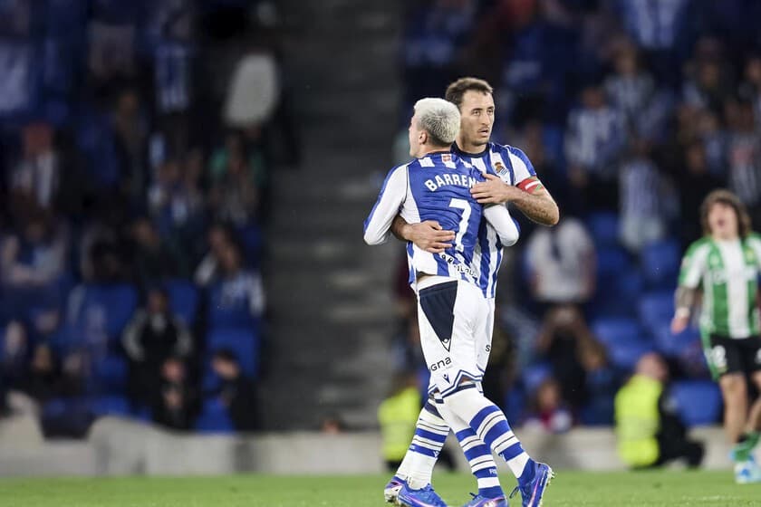 Jugadores de fútbol disputando un balón en un partido de LaLiga con el marcador de fondo.