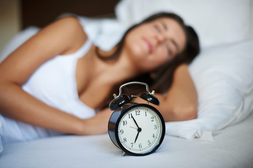 Persona durmiendo plácidamente en una cama minimalista, con luz tenue y reloj marcando las 8 horas