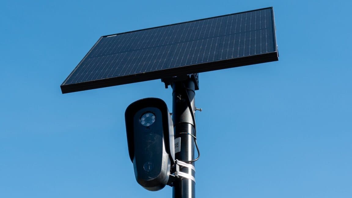 Cámara de vigilancia en un poste de luz con un automóvil pasando