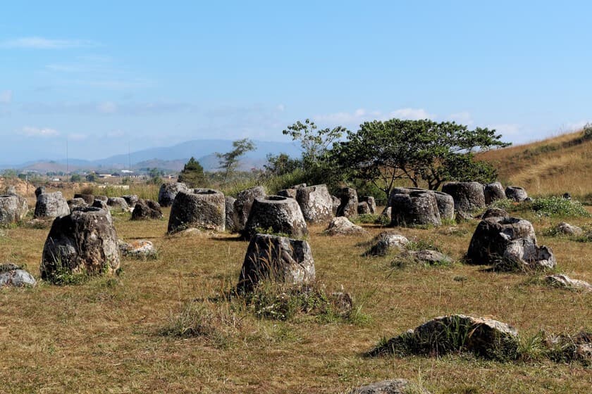 Fotografía de una jarra gigante de piedra en la llanura de Laos, con vegetación alrededor.