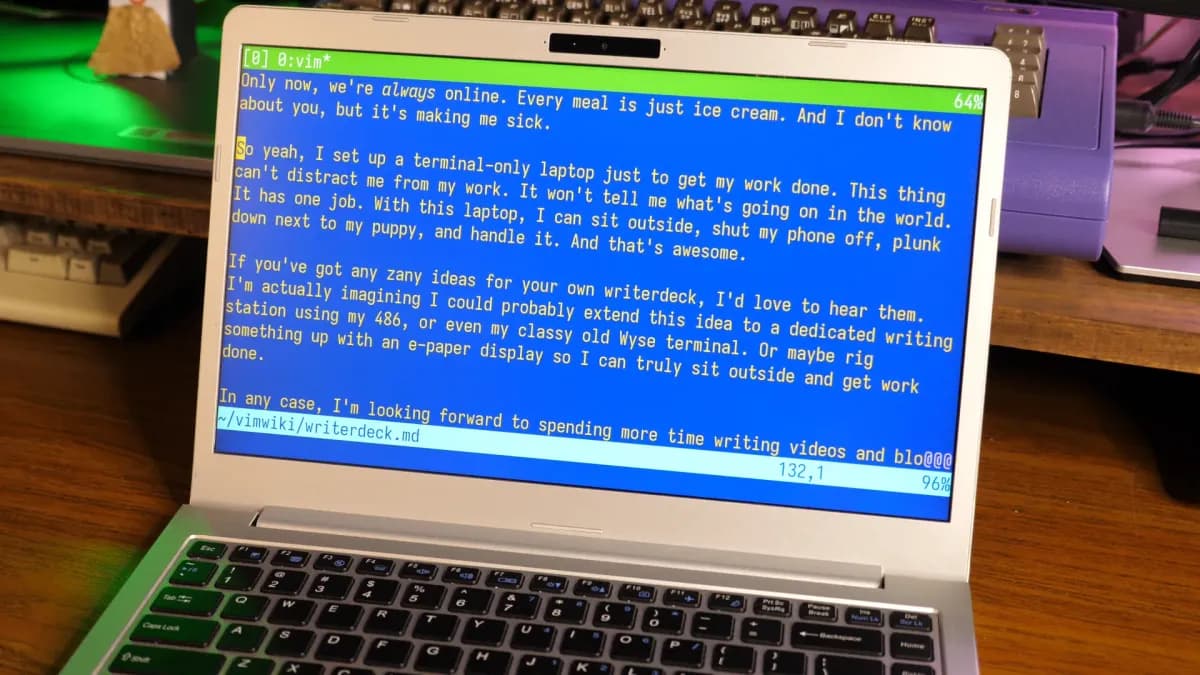 Un ordenador portátil pequeño con pantalla monocromática y teclado mecánico, sobre una mesa de madera, con una taza de c