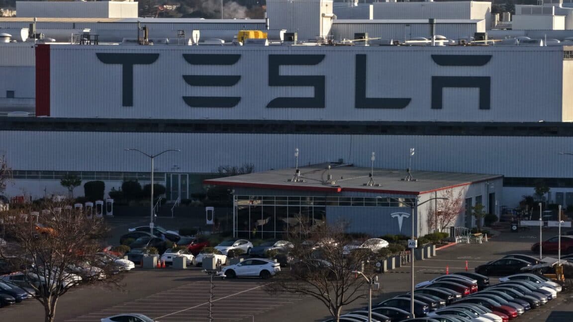 Fotografía de la fachada de una fábrica de Tesla con el logo de la compañía, al fondo un cielo nublado