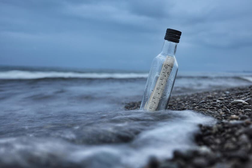 Botella de vidrio con un mensaje enrollado en su interior, semienterrada en la arena de una playa caribeña.