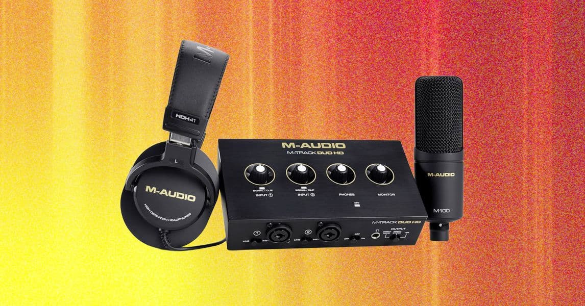Interfaz de audio M-Audio M Track Duo HD sobre una mesa de madera, con micrófono y auriculares conectados.