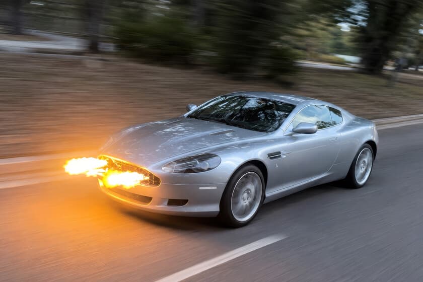Aston Martin DB9 plateado con llamas saliendo de la parrilla frontal, de noche