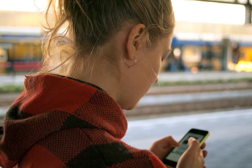 Adolescente con auriculares mirando una tablet con interfaz de chat de IA, fondo neutro