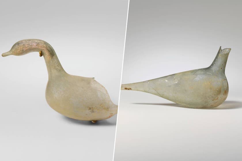 Réplica de una paloma de vidrio romana para perfume, con el cuello alargado y frágil, sobre fondo oscuro.