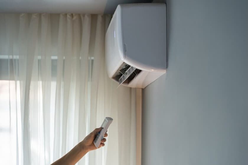 Persona durmiendo en una cama con un termómetro digital marcando 18°C junto a un control de aire acondicionado