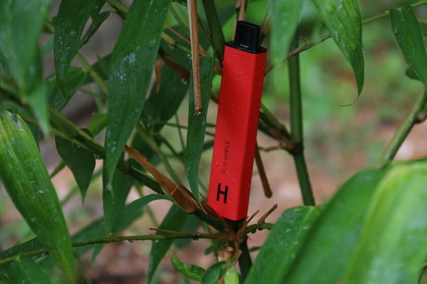 Persona usando un vaper con expresión seria, fondo oscuro