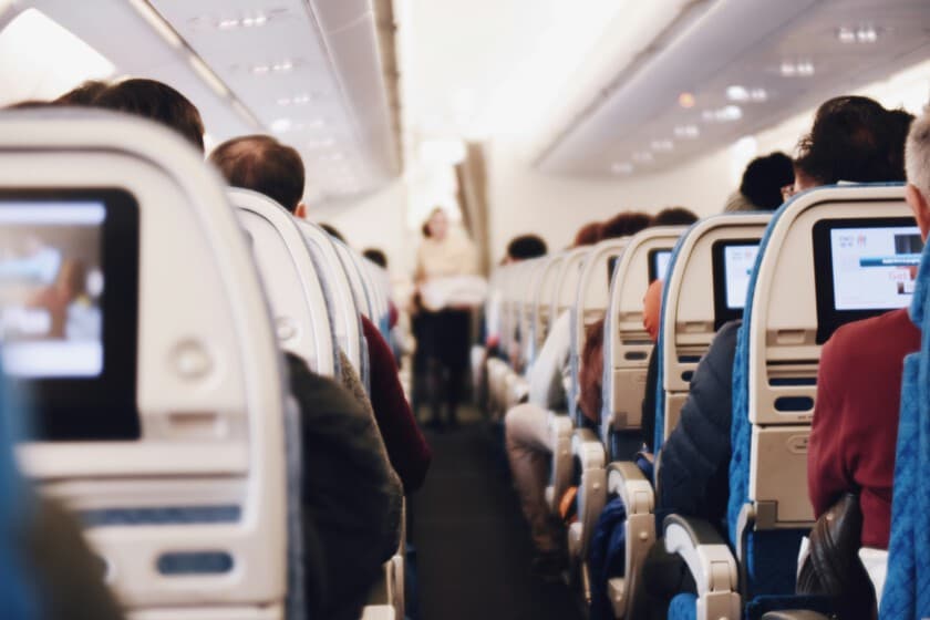 Pasajeros en un aeropuerto con maletas de mano, algunos revisando sus teléfonos