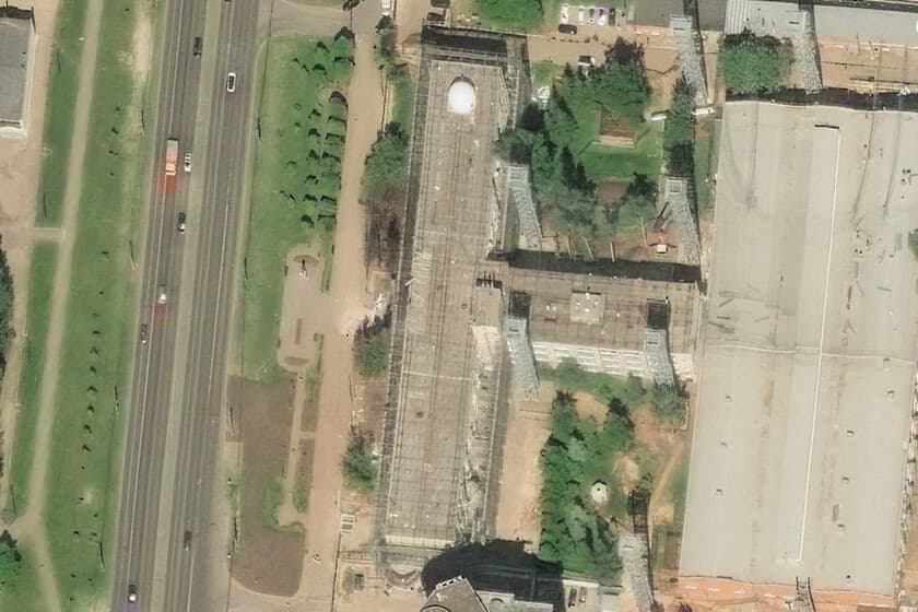 Imagen satelital de un edificio cubierto por una estructura metálica tipo jaula, con un dron sobrevolando.