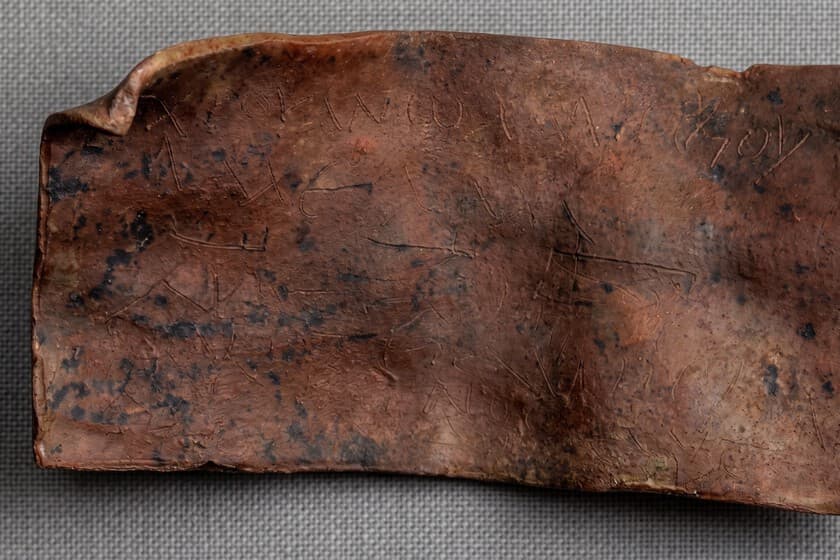 Primer plano de una tablilla de plomo enrollada con inscripciones griegas antiguas, iluminada sobre fondo oscuro