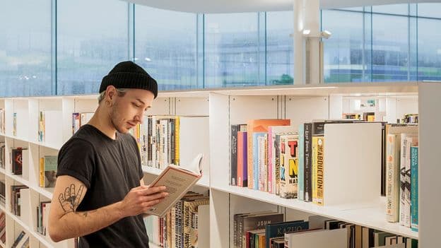 Interior de una biblioteca finlandesa moderna con estanterías de herramientas y una máquina de coser en primer plano