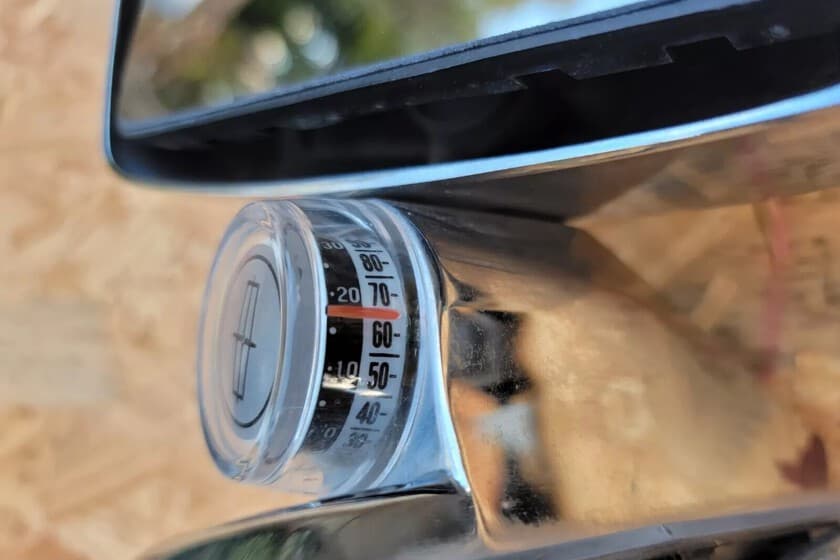 Retrovisor de coche antiguo con un termómetro analógico pegado al cristal, enfoque en el detalle del invento casero.